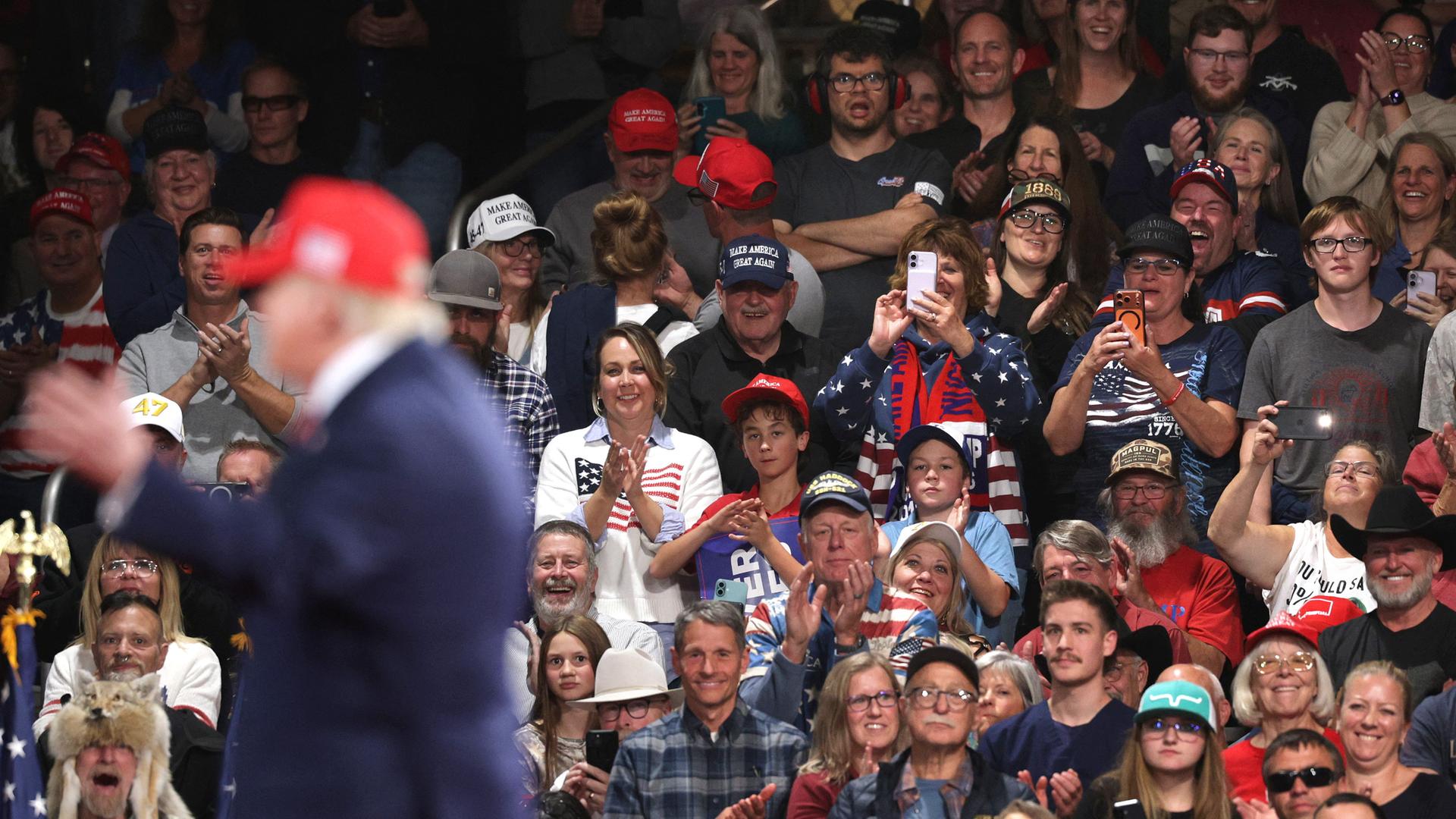 Anhänger sitzen bei einer Wahlkampfveranstaltung anläslich der Midterms in der Majestic Valley Arena in Kalispell; im Vordergrund steht US-Präsident Donald Trump zu sehen (14. Oktober 2026, Montana, USA) Anhänger sitzen bei einer Wahlkampfveranstaltung anläslich der Midterms in der Majestic Valley Arena in Kalispell; im Vordergrund steht US-Präsident Donald Trump zu sehen (14. Oktober 2026, Montana, USA)