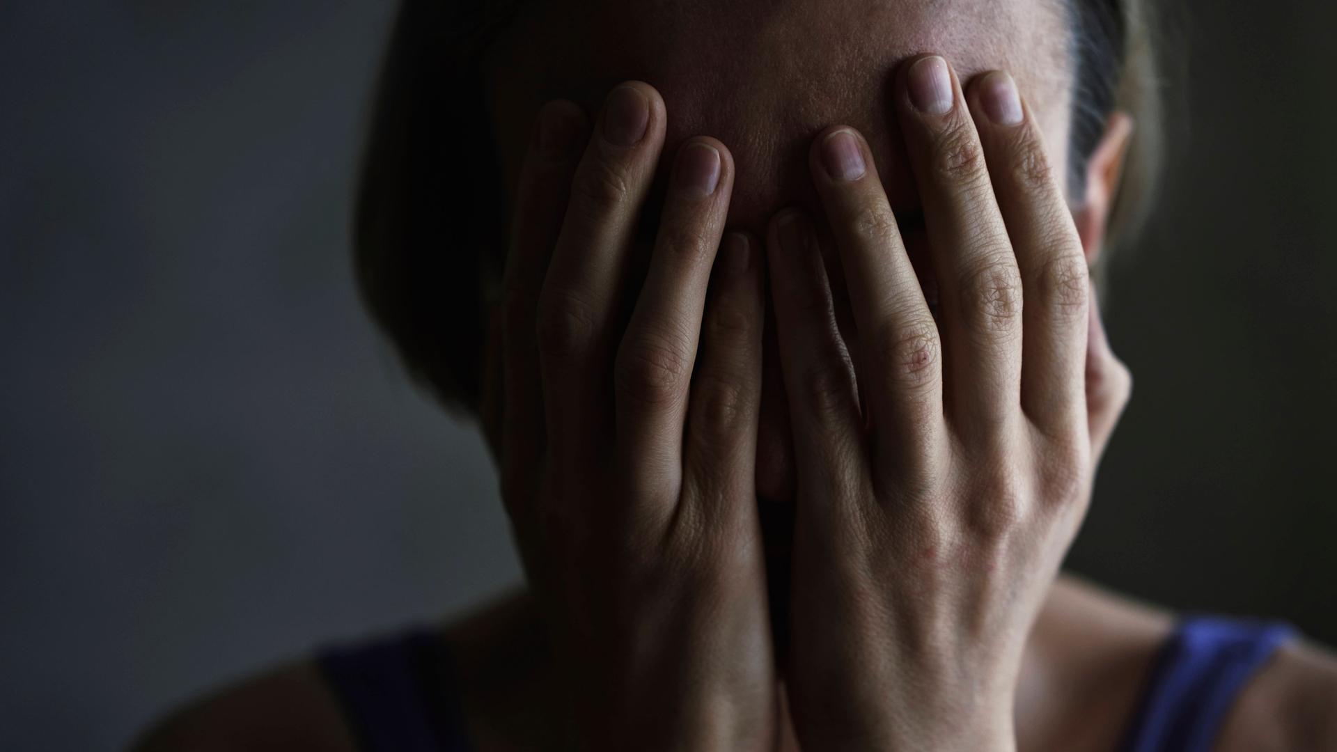 Foto des Kopfes einer Frau, die beide Hände vor ihr Gesicht hält