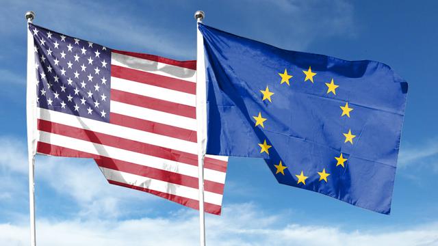 Foto der Flaggen der EU und der USA, die nebeneinander vor blauem Himmel im Wind flattern