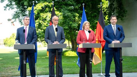 Söder, Merz, Bas und Klingbeil stehen an Redepulten. Hinter ihnen stehen die Ndeutsche Nationalfahne und die EU-Flagge.