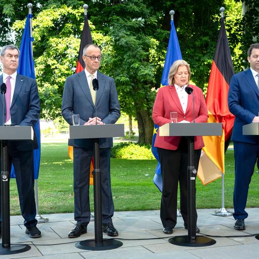 Söder, Merz, Bas und Klingbeil stehen an Redepulten. Hinter ihnen stehen die Ndeutsche Nationalfahne und die EU-Flagge.