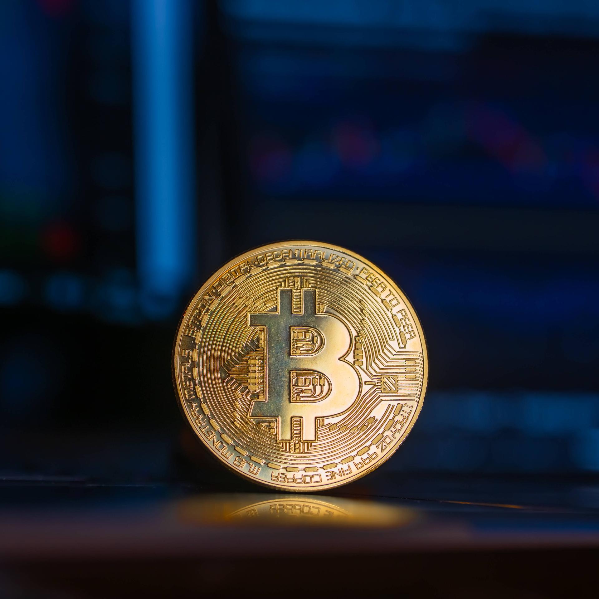 Eine goldene Bitcoin-Münze steht aufrecht vor einem Computer-Bildschirm.