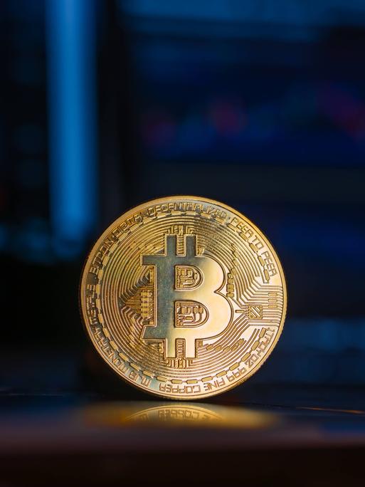 Eine goldene Bitcoin-Münze steht aufrecht vor einem Computer-Bildschirm.