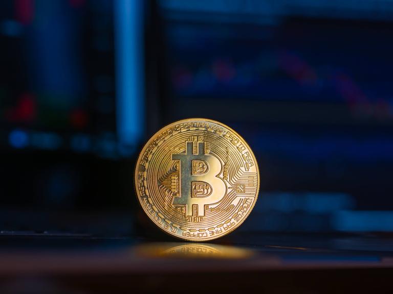 Eine goldene Bitcoin-Münze steht aufrecht vor einem Computer-Bildschirm.