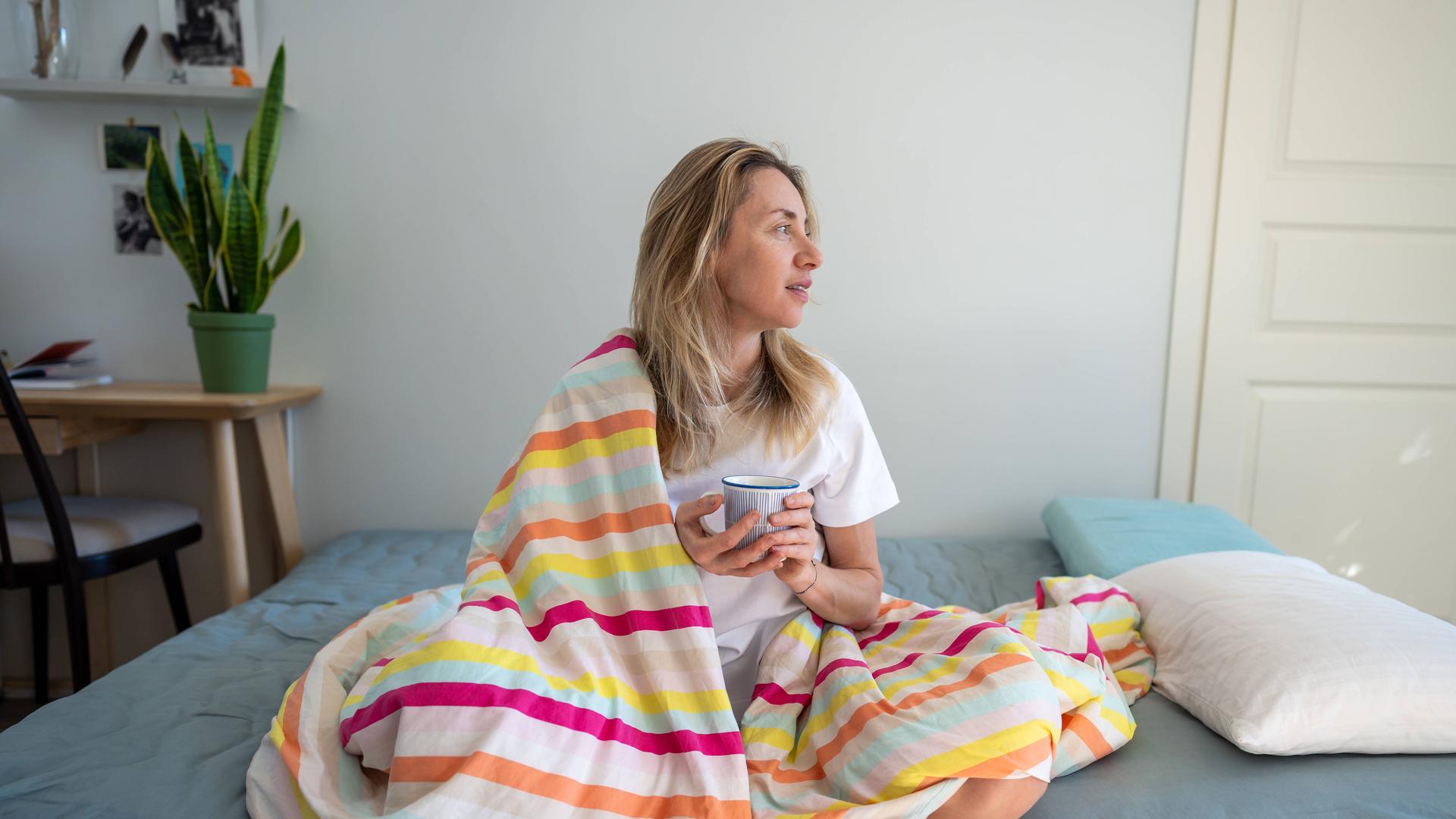 Entspannte Frau im Bett, die Kaffee und Kontemplation genießt, sich an einem faulen Morgen ausruht.