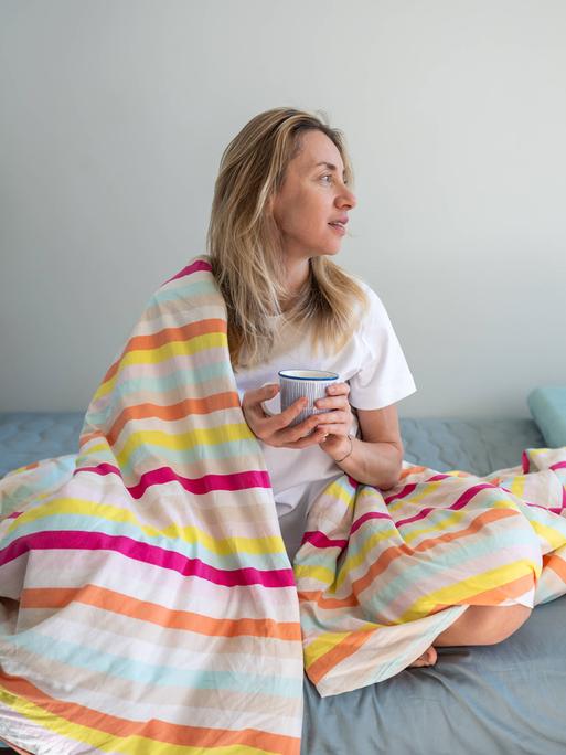 Entspannte Frau im Bett, die Kaffee und Kontemplation genießt, sich an einem faulen Morgen ausruht.