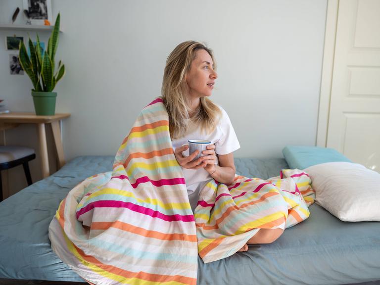 Entspannte Frau im Bett, die Kaffee und Kontemplation genießt, sich an einem faulen Morgen ausruht.