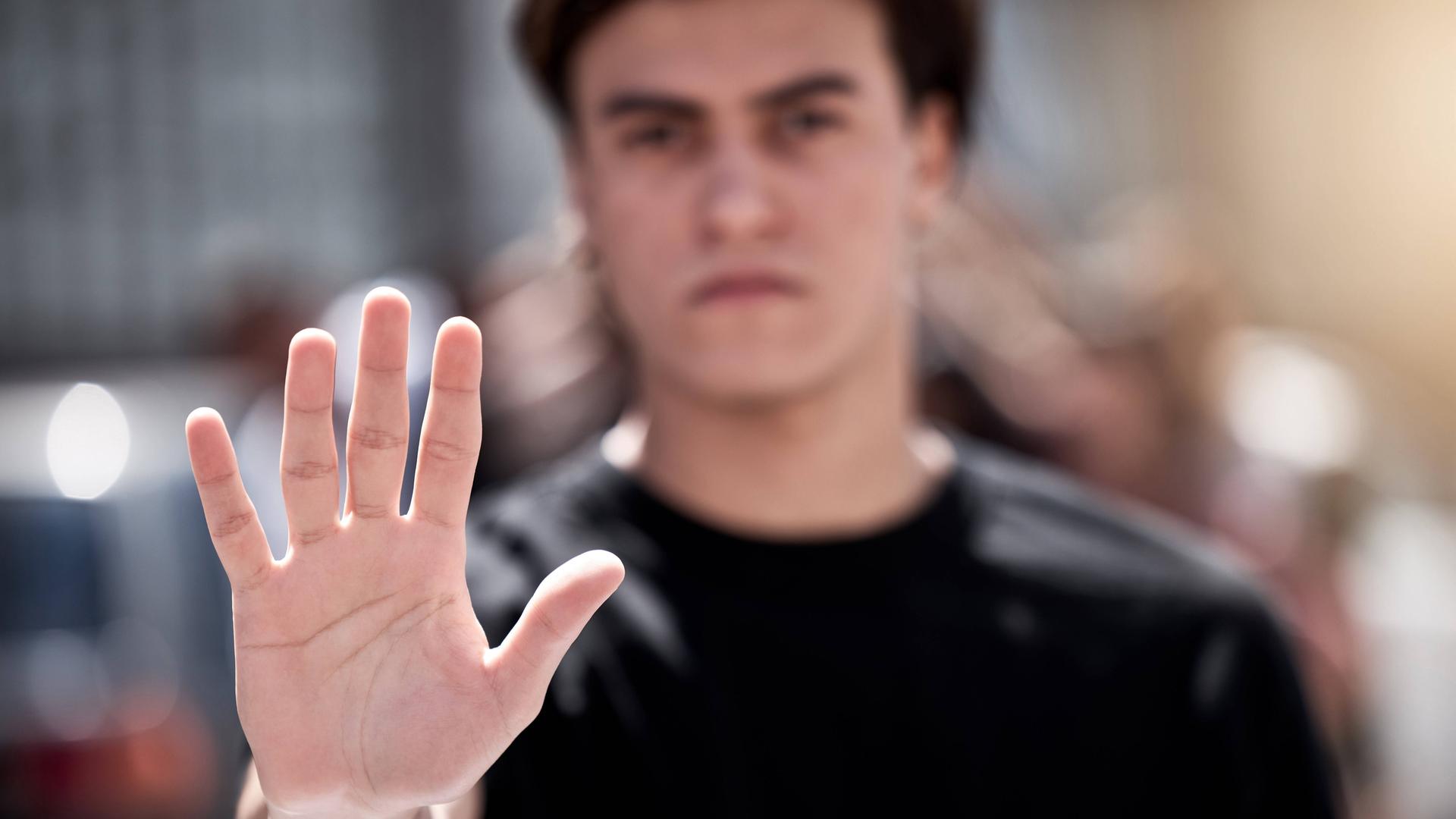 Foto eines jungen Mannes, der die Hand hebt und so "Stopp" signalisiert - Die Hand vorne ist scharf, der Mann dahinter unscharf. Foto eines jungen Mannes, der die Hand hebt und so "Stopp" signalisiert - Die Hand vorne ist scharf, der Mann dahinter unscharf.