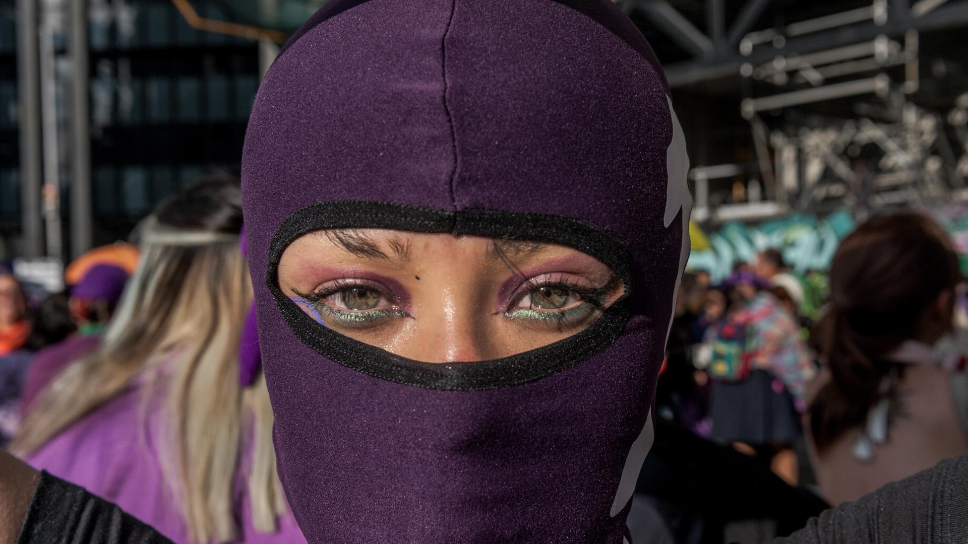 Bei einer Demonstration zum internationalen Frauentag in Kolumbiens Hauptstadt Bogota trägt eine Frau eine lilafarbene Mütze über ihrem Kopf, die auch ihr Gesicht verdeckt. Man sieht nur ihre Augen. Bei einer Demonstration zum internationalen Frauentag in Kolumbiens Hauptstadt Bogota trägt eine Frau eine lilafarbene Mütze über ihrem Kopf, die auch ihr Gesicht verdeckt. Man sieht nur ihre Augen.
