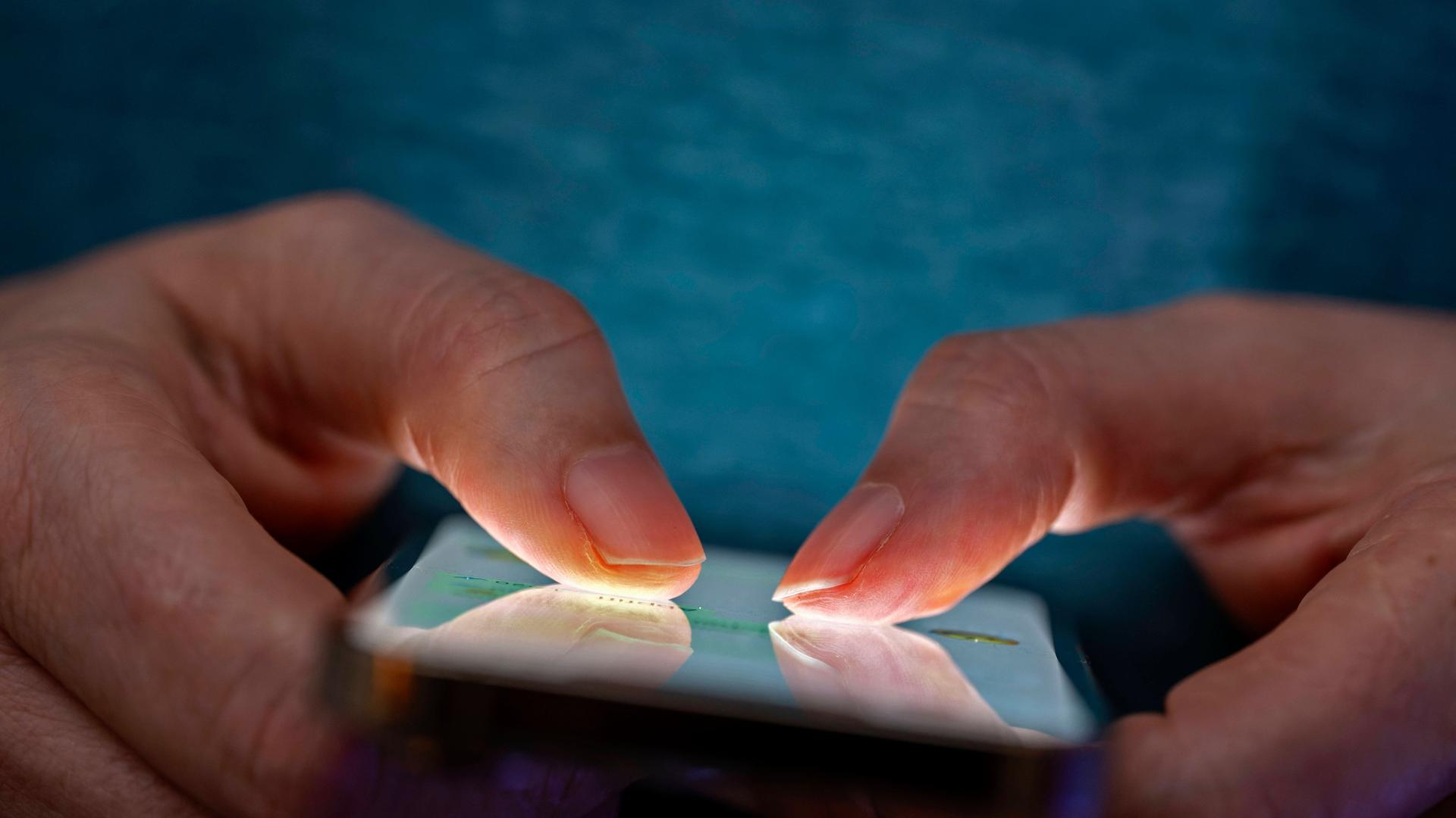 Eine Person hält in seinen Händen ein Handy und tippt darauf mit den beiden Daumen.