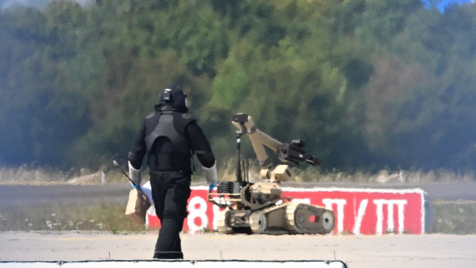 Das Bild zeigt einen Roboter, der auf einem Flughafen-Feld von einem Sprengstoff-Experten gesteuert wird. 