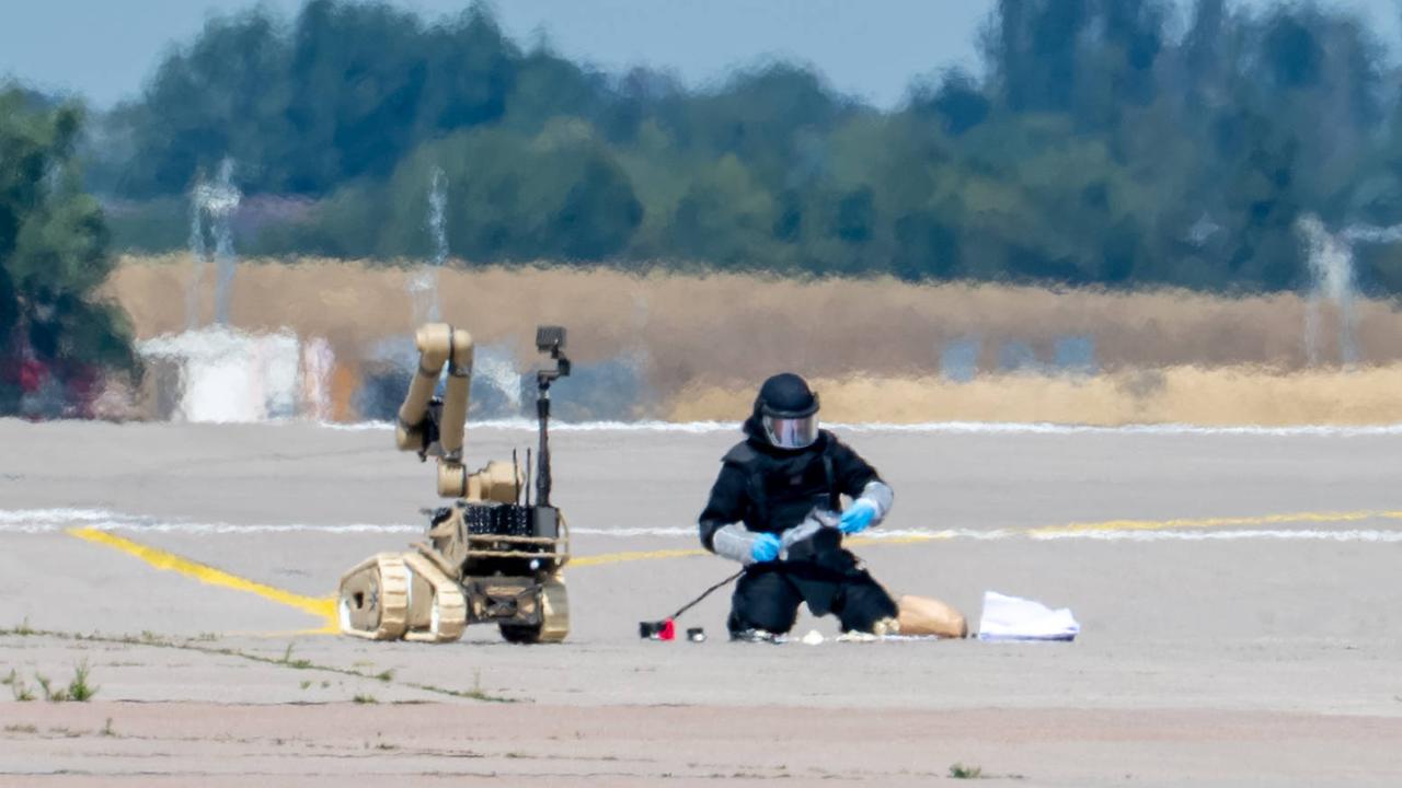 Ein Kriminalbeamter entschärft die Drohne am Flughafen Leipzig/Halle. Neben ihm steht ein Sprengstoffroboter. Der Beamte trägt Schutzkleidung und einen Helm mit Visier.