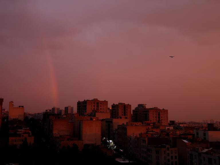 In der iranischen Hauptstadt Teheran geht gerade die Sonne auf. Über den Häusern der Stadt hängt eine dichte, rosafarbene Wolkendecke. Das Bild wurde am 10.12.25 aufgenommen.