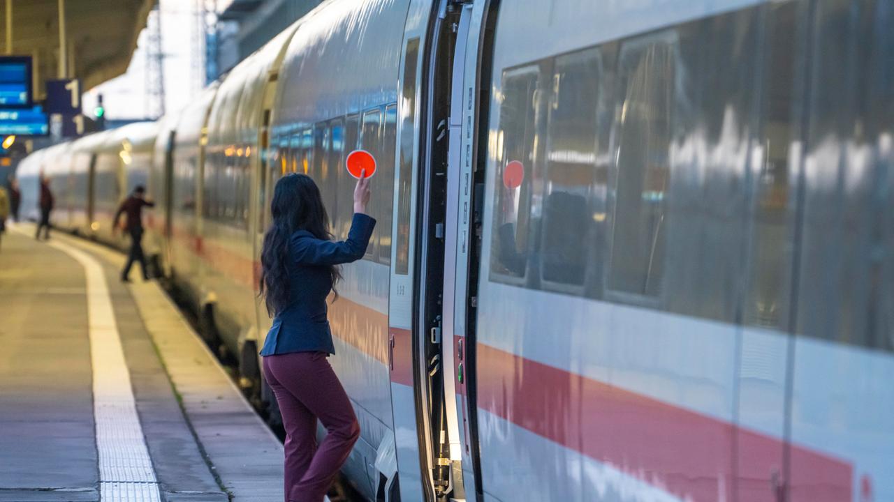 Mitarbeiterin der Deutsche Bahn steht an der offenen Tür eines ICEs und hält den Abfahrstab in die Höhe (Hauptbahnhof Essen, 11.11.2025)