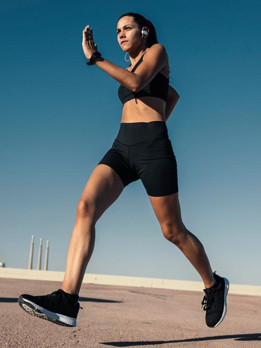 Eine junge Frau joggt draußen vor blauem Himmel. Sie wirkt sehr fit und dynamisch. Im Hintergrund sind Schornsteine zu sehen. Eine junge Frau joggt draußen vor blauem Himmel. Sie wirkt sehr fit und dynamisch. Im Hintergrund sind Schornsteine zu sehen.