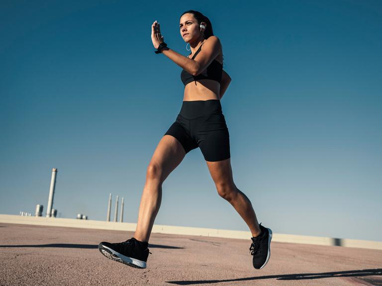 Eine junge Frau joggt draußen vor blauem Himmel. Sie wirkt sehr fit und dynamisch. Im Hintergrund sind Schornsteine zu sehen. Eine junge Frau joggt draußen vor blauem Himmel. Sie wirkt sehr fit und dynamisch. Im Hintergrund sind Schornsteine zu sehen.