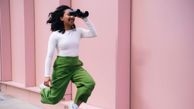 Eine Frau schaut durch ein Fernglas und bewegt sich dabei nach vorne.