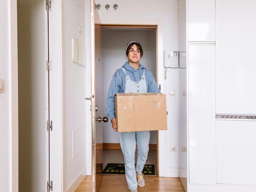 Eine junge Frau trägt einen Umzugskarton in eine Wohnung