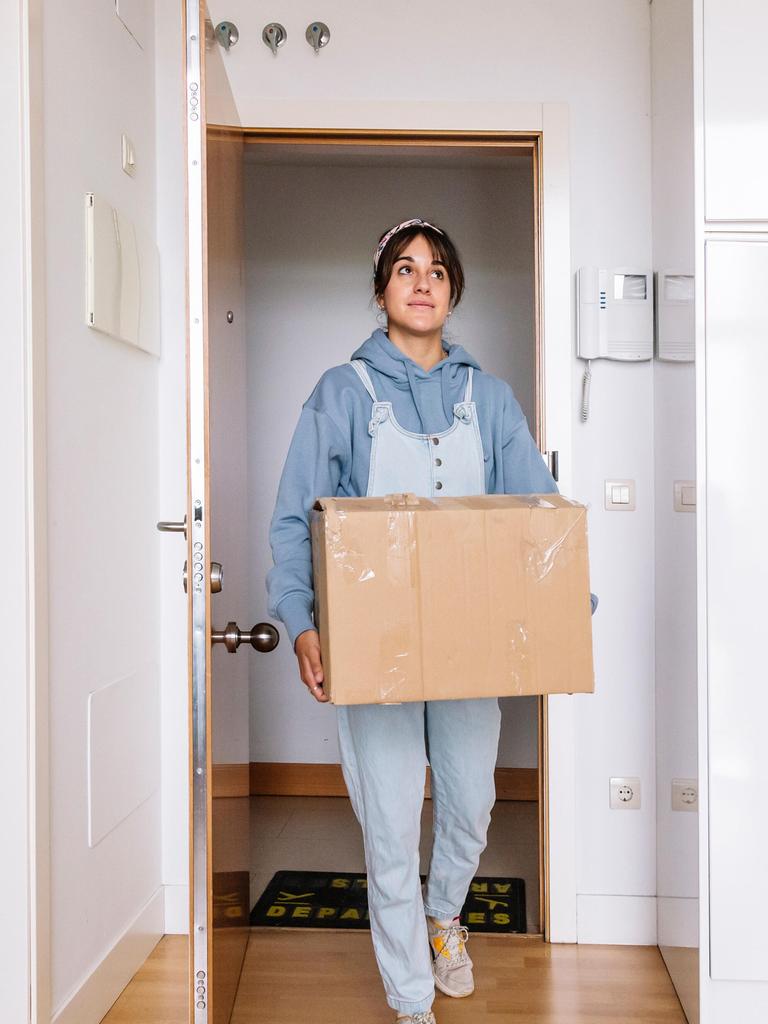 Eine junge Frau trägt einen Umzugskarton in eine Wohnung