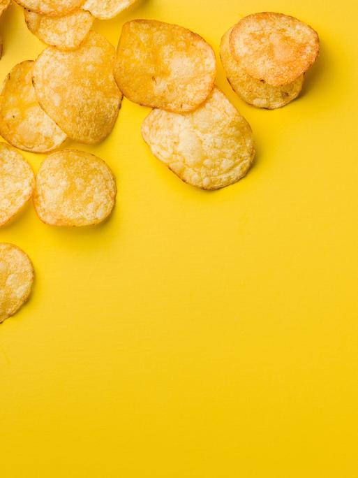 Eine Handvoll Kartoffelchips liegen auf einem gelben Tisch.