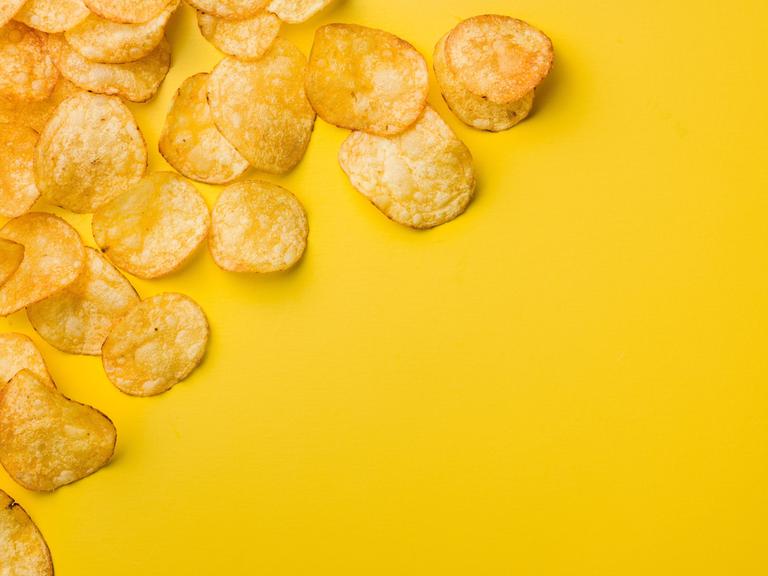 Eine Handvoll Kartoffelchips liegen auf einem gelben Tisch.