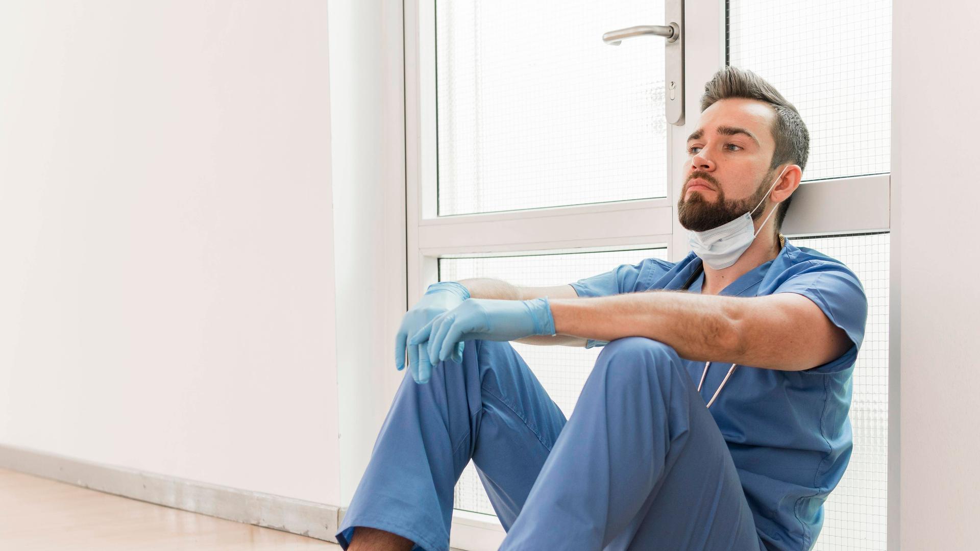 Krankenpfleger sitzt erschöpft auf dem Boden