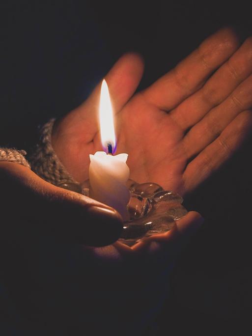 Foto einer brennende Kerze in weiblichen Händen bei Nacht