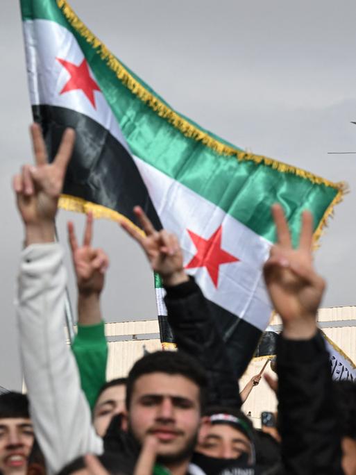 Ein Hubschrauber fliegt über eine Menschenmenge. Das Siegeszeichen und Flaggen werden gezeigt. Es handelt sich um Feierlichkeiten zum Jahrestag des Sturzes des Machthabers Baschar al-Assad in der syrischen Hauptstadt Damaskus (8.12.2025, Syrien) Ein Hubschrauber fliegt über eine Menschenmenge. Das Siegeszeichen und Flaggen werden gezeigt. Es handelt sich um Feierlichkeiten zum Jahrestag des Sturzes des Machthabers Baschar al-Assad in der syrischen Hauptstadt Damaskus (8.12.2025, Syrien)