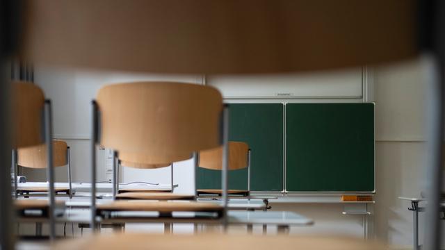 Stühle stehen auf Tischen in einem Klassenraum mit grüner Tafel im Hintergrund
