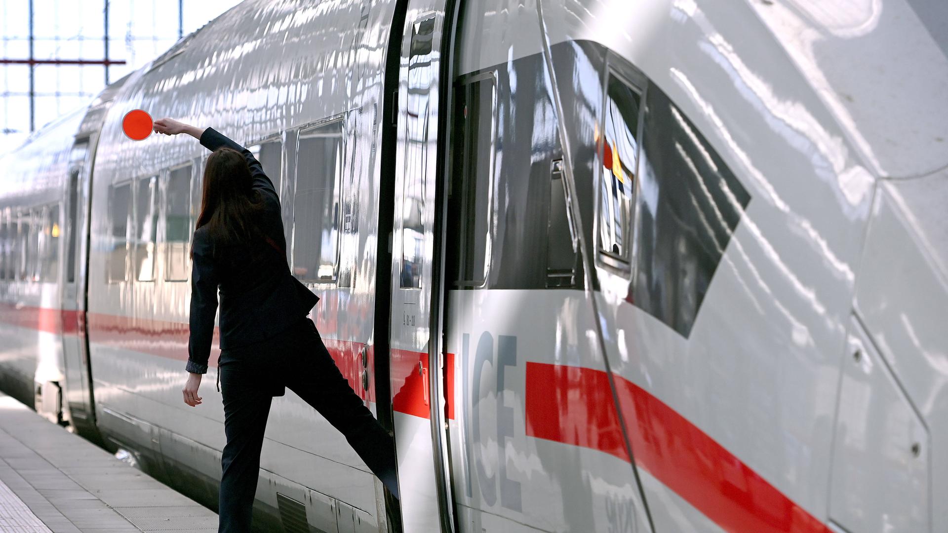 Eine Bahn-Mitarbeiterin steht mit einem Fuß auf dem Gleis, mit dem anderen Fuß im ICE. Der Zug ist im Begriff, vom Hauptbahnhof München abzufahren.