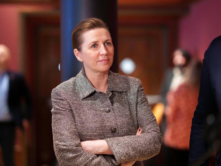 Die dänische Ministerpräsidentin Mette Fredriksen steht in einem Raum, im Hintergrund sind Personen erkennbar. Sie blickt nach rechts. Sie trägt eine braune Stoffjacke. Die dänische Ministerpräsidentin Mette Fredriksen steht in einem Raum, im Hintergrund sind Personen erkennbar. Sie blickt nach rechts. Sie trägt eine braune Stoffjacke.