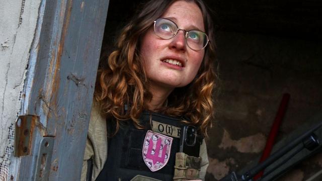 Foto von Anna Elsbernd, die mit ihrer Organisation "Universal Aid Ukraine" in der Ukraine Menschen aus Kriegsgebieten evakuiert: Sie sitzt mit einer Schutzweste bekleidet in einem Gebäude und schaut durch eine Türöffnung besorgt in den Himmel.