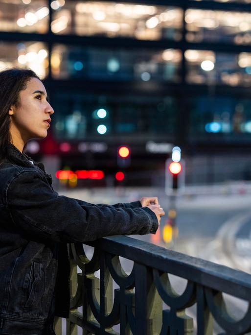 Eine Frau blickt in einer Stadt an einer breiten Kreuzung von einer Brücke in die Ferne. Eine Frau blickt in einer Stadt an einer breiten Kreuzung von einer Brücke in die Ferne.
