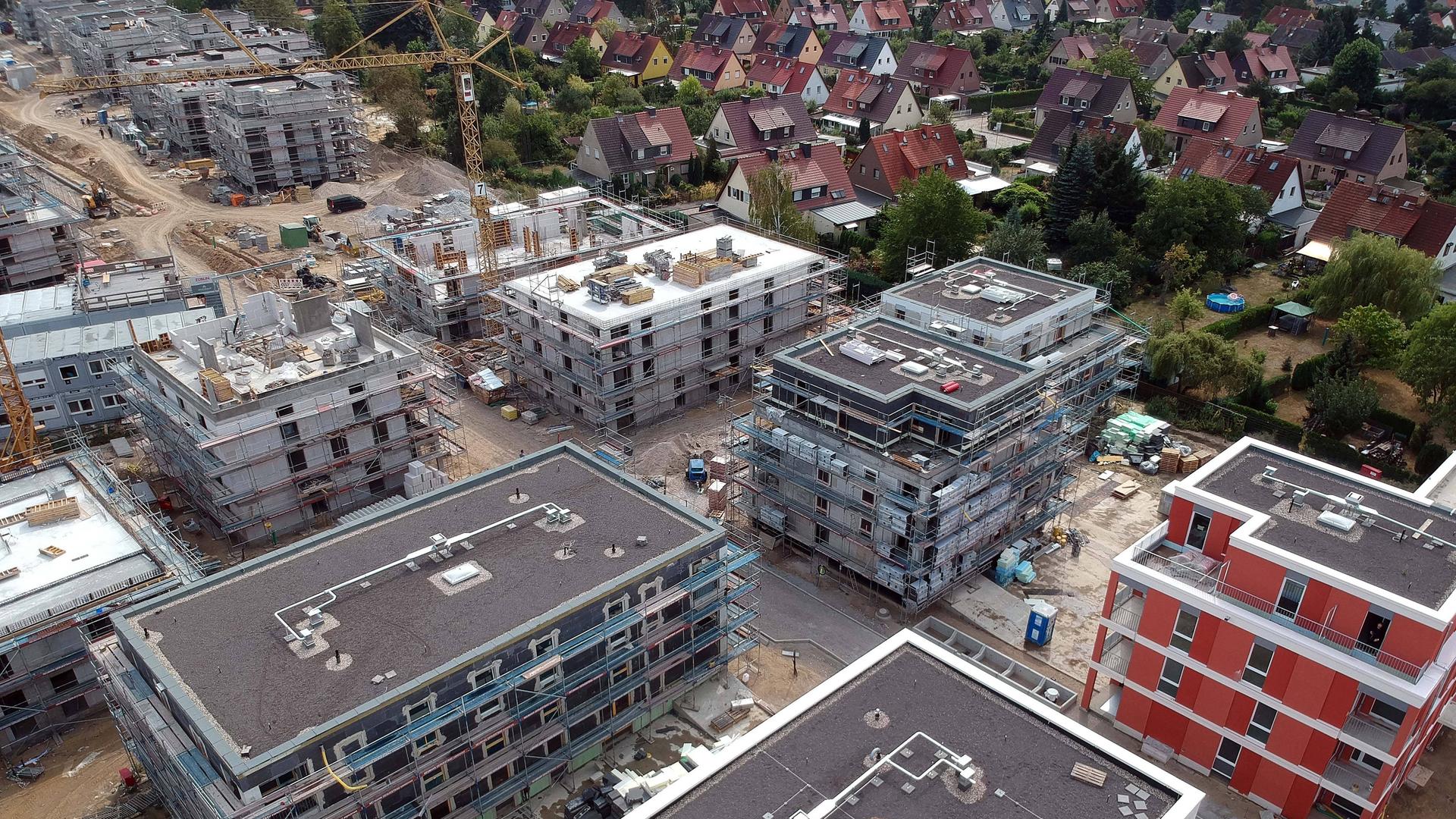 Baustelle für einen Neubau von Mehrfamilienhäusern mit Kran im Hintergrund und Einfamilienhäuser an der Seite Baustelle für einen Neubau von Mehrfamilienhäusern mit Kran im Hintergrund und Einfamilienhäuser an der Seite