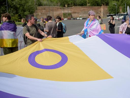 Auf einer Demonstration in Rom tragen Teilnehmende eine große Flagge mit dem Symbol der Inter*-Bewegung, einem lila Kreis auf gelbem Hintergrund. Die Flagge ist für Menschen, die sich als intergeschlechtlich identifizieren.