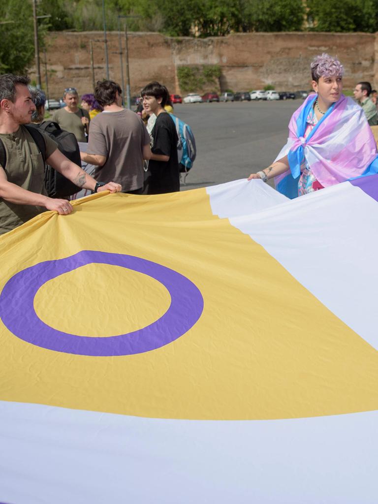 Auf einer Demonstration in Rom tragen Teilnehmende eine große Flagge mit dem Symbol der Inter*-Bewegung, einem lila Kreis auf gelbem Hintergrund. Die Flagge ist für Menschen, die sich als intergeschlechtlich identifizieren.