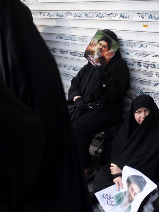 Eine verschleierte Iranerin lehnt sich während einer Jubeldemonstration für Mojtaba Khamenei Anfang März 2026 an die Jalousie eines Geschäfts.