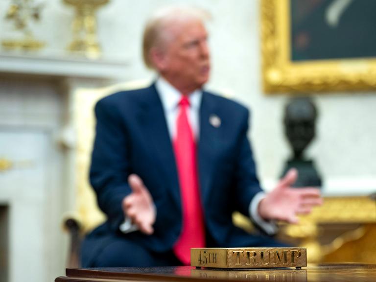 Vergoldeter Untersetzer mit der Aufschrift "45th" und "Trump". Im Hintergrund US-präsident Donald Trump Vergoldeter Untersetzer mit der Aufschrift "45th" und "Trump". Im Hintergrund US-präsident Donald Trump