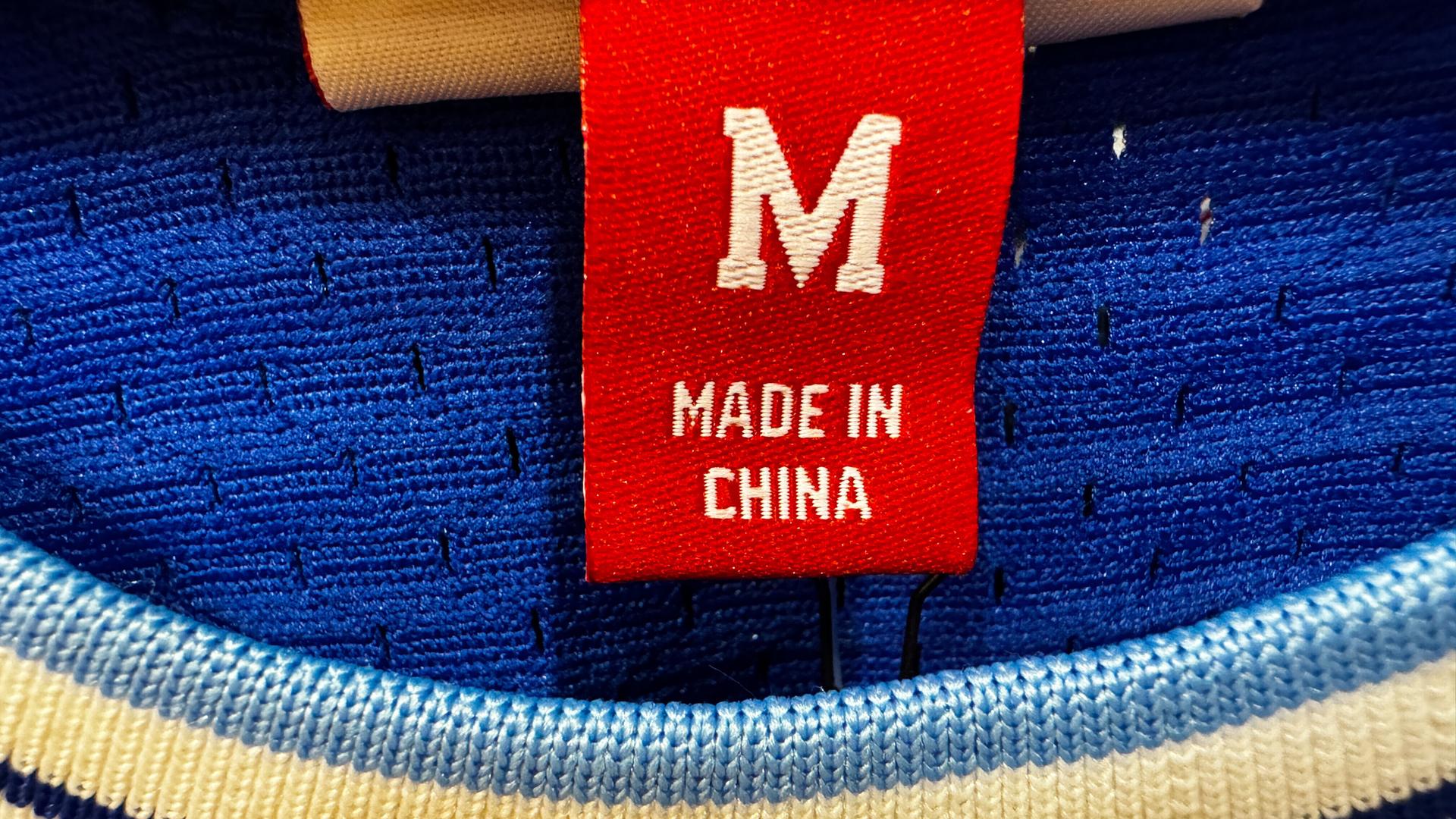 In der Nahaufnahme ist ein rotes Etikett mit der weißen Aufschrift „Made in China“ und der Größe M in einem Halsausschnitt eines Strickpullis zu sehen.