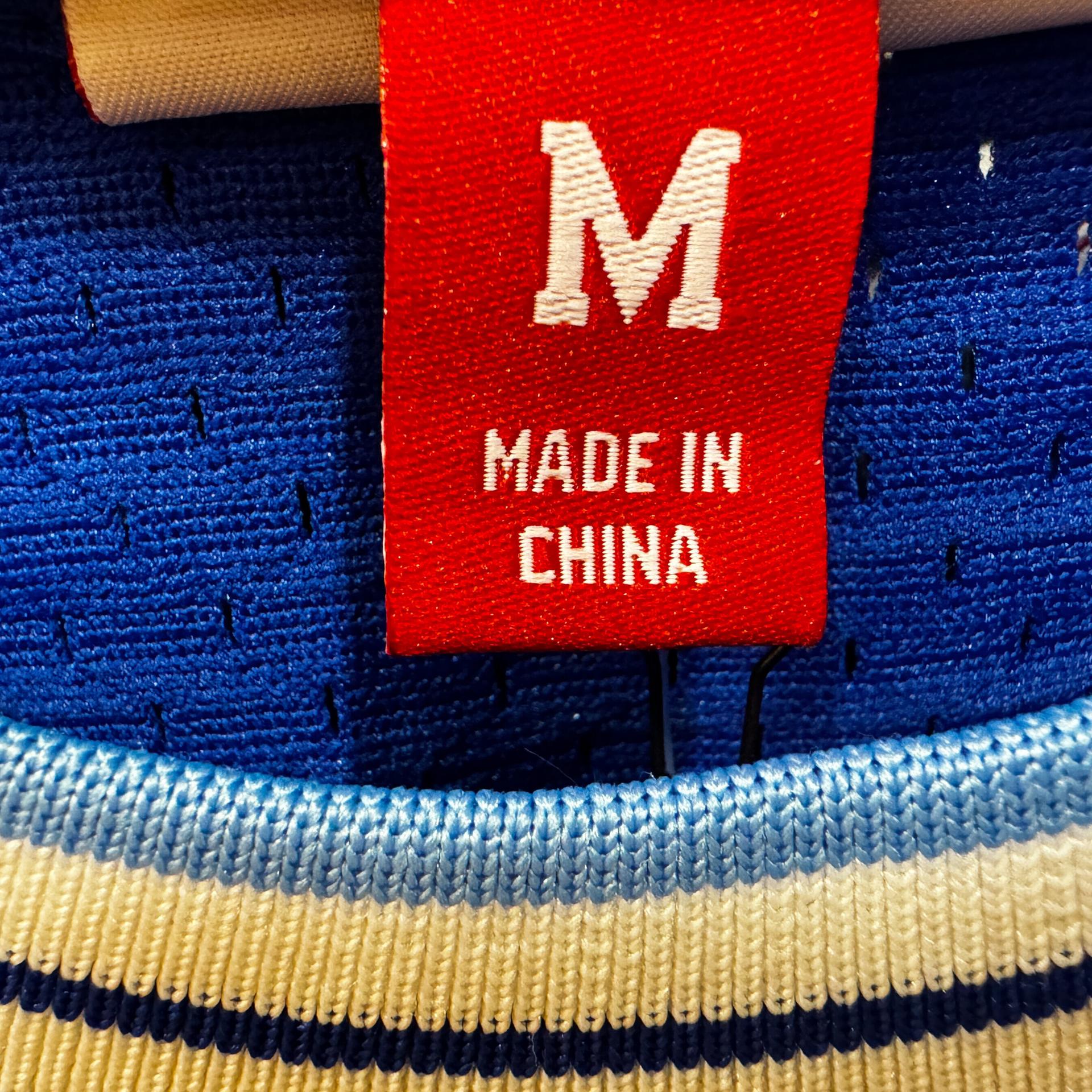 In der Nahaufnahme ist ein rotes Etikett mit der weißen Aufschrift „Made in China“ und der Größe M in einem Halsausschnitt eines Strickpullis zu sehen.