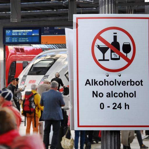Fotomontage: Menschen in einem Bahnhof, großes Schild "Alkoholverbot 0-24h"