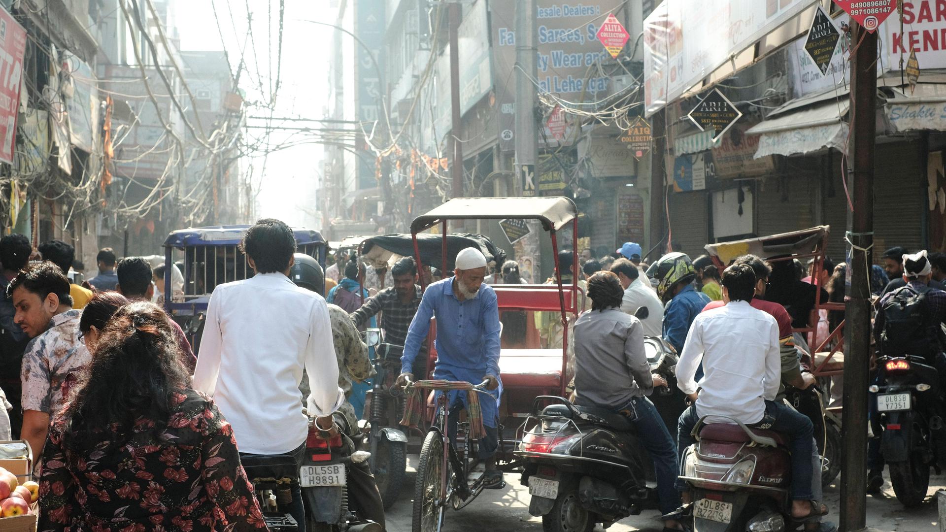 Eine Straßenszene in Neu Delhi: Menschen und eine Rikscha tummeln sich auf der Straße