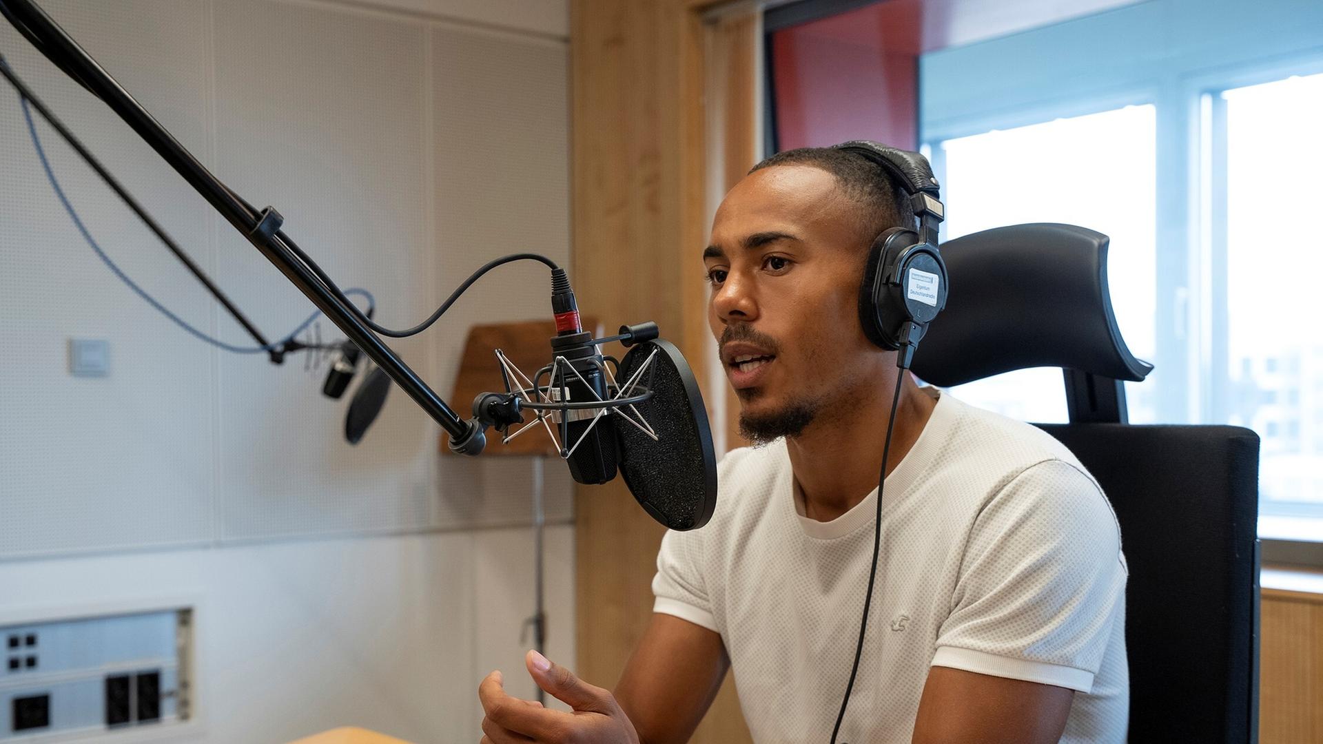 Der Fußballspieler Robin Afamefuna sitzt im Dlf Nova-Studio am Mikrofon und hat einen Kopfhörer auf.
