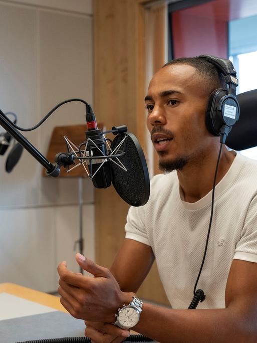 Der Fußballspieler Robin Afamefuna sitzt im Dlf Nova-Studio am Mikrofon und hat einen Kopfhörer auf.