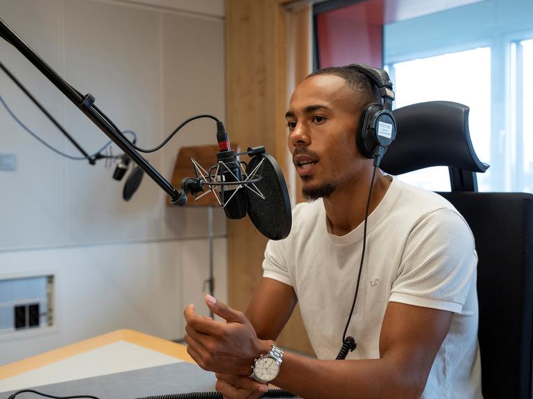 Der Fußballspieler Robin Afamefuna sitzt im Dlf Nova-Studio am Mikrofon und hat einen Kopfhörer auf.