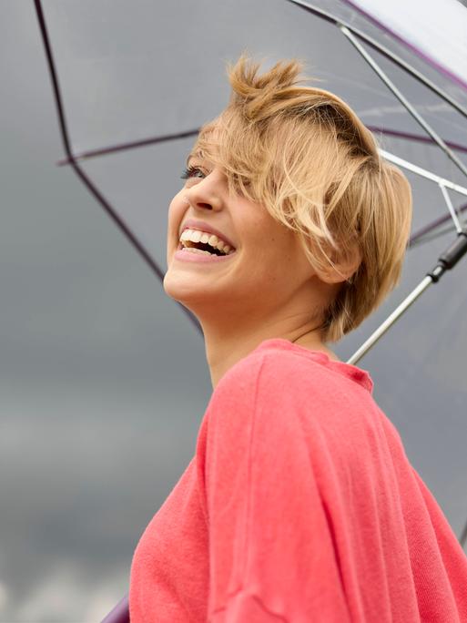 Eine lächelnde junge Frau unter einem Regenschirm. Dunkle Wolken am Himmel. Eine lächelnde junge Frau unter einem Regenschirm. Dunkle Wolken am Himmel.