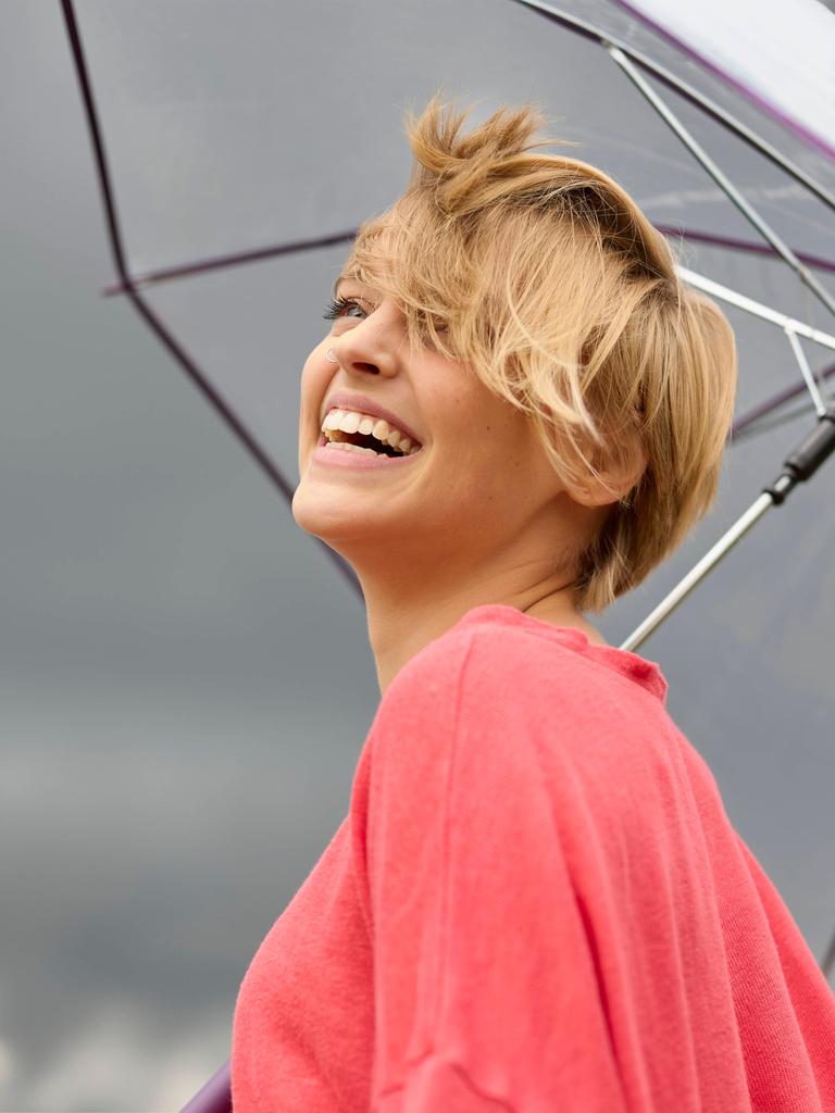 Eine lächelnde junge Frau unter einem Regenschirm. Dunkle Wolken am Himmel. Eine lächelnde junge Frau unter einem Regenschirm. Dunkle Wolken am Himmel.