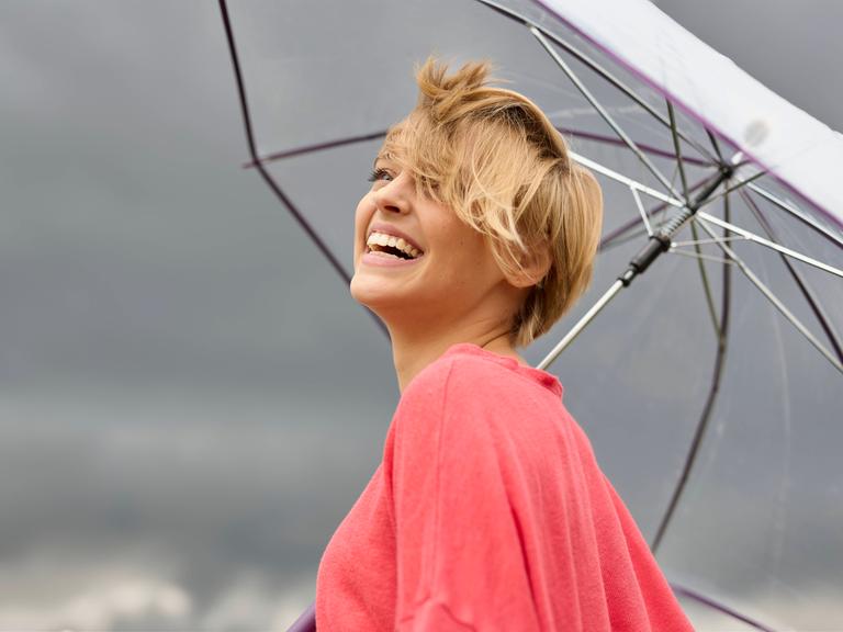 Eine lächelnde junge Frau unter einem Regenschirm. Dunkle Wolken am Himmel. Eine lächelnde junge Frau unter einem Regenschirm. Dunkle Wolken am Himmel.