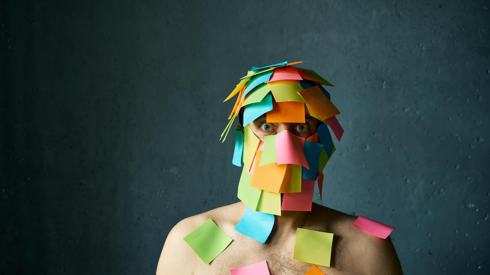 Ein Mann hat viele Post-its-Notes im Gesicht und auf den Schultern kleben und schaut gestresst