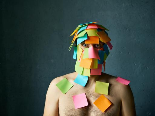 Ein Mann hat viele Post-its-Notes im Gesicht und auf den Schultern kleben und schaut gestresst
